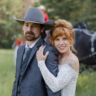 Man in cowboy hat and suit, woman in white lace dress, embracing.
