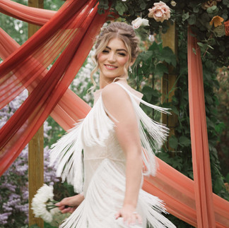 Smiling woman in white fringed dress at outdoor celebration.