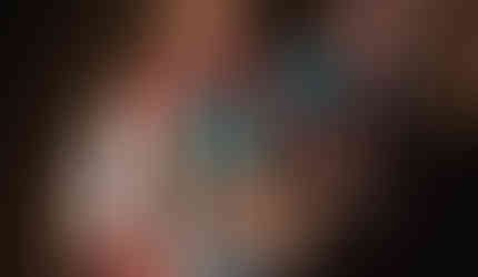 Indigenous person in colorful traditional regalia holding a rattle and feather fan.