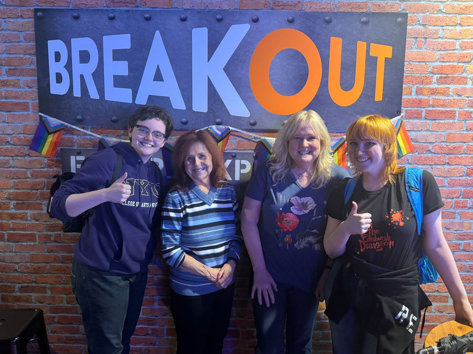 Group of friends at Breakout, thumbs up near sign with rainbow flags.
