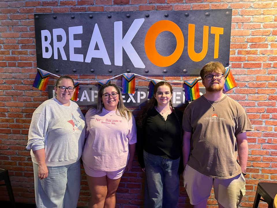 Four people smiling in front of a sign that reads BREAKOUT. Cafe Experience.