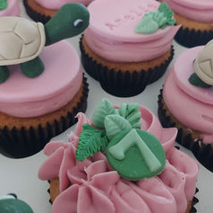 Pink frosted cupcakes with green turtle and leaf toppers in a box.