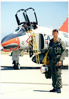 Dana Shute, President of Top Gun Traders Edge, former Navy pilot, standing in front of an F-4 fighter jet during military service