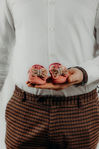 Werdender Vater hält Babyschuhe der Tochter beim Babybauchshooting in den Händen.