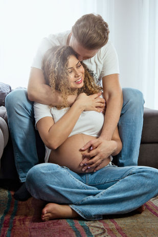 Werdende Eltern beim Homeshooting: Frau lehnt sich an ihren Mann, beide halten den Babybauch.