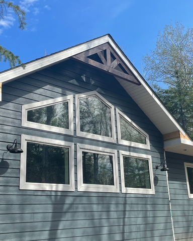 New cabin build exterior with dark grey siding, large windows, and wood gable by Flip Flop Construction in Manitoba