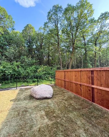 Cedar privacy fence with natural boulder feature in a landscaped backyard by Flip Flop Construction in Manitoba