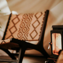Lounge chair by lit log burner in a glamping tipi