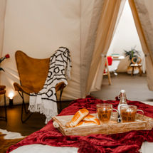 Sitting Bull glamping tipi interior with breakfast in bed and a glimpse through to the connected en suite with roll-top bath.