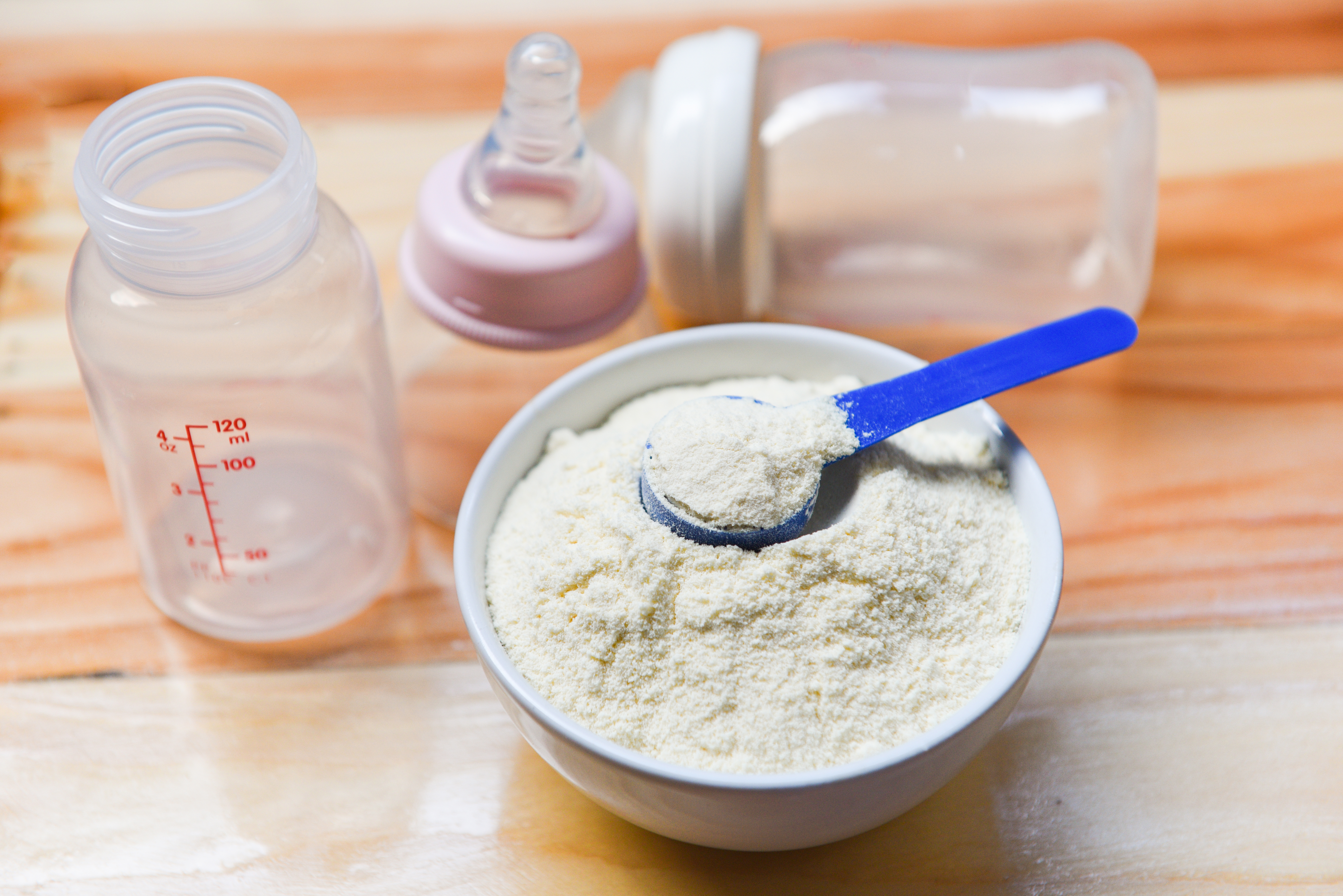 Bowl of powdered infant formula with a scoop, alongside baby bottles, emphasizing the role of soya protein concentrate