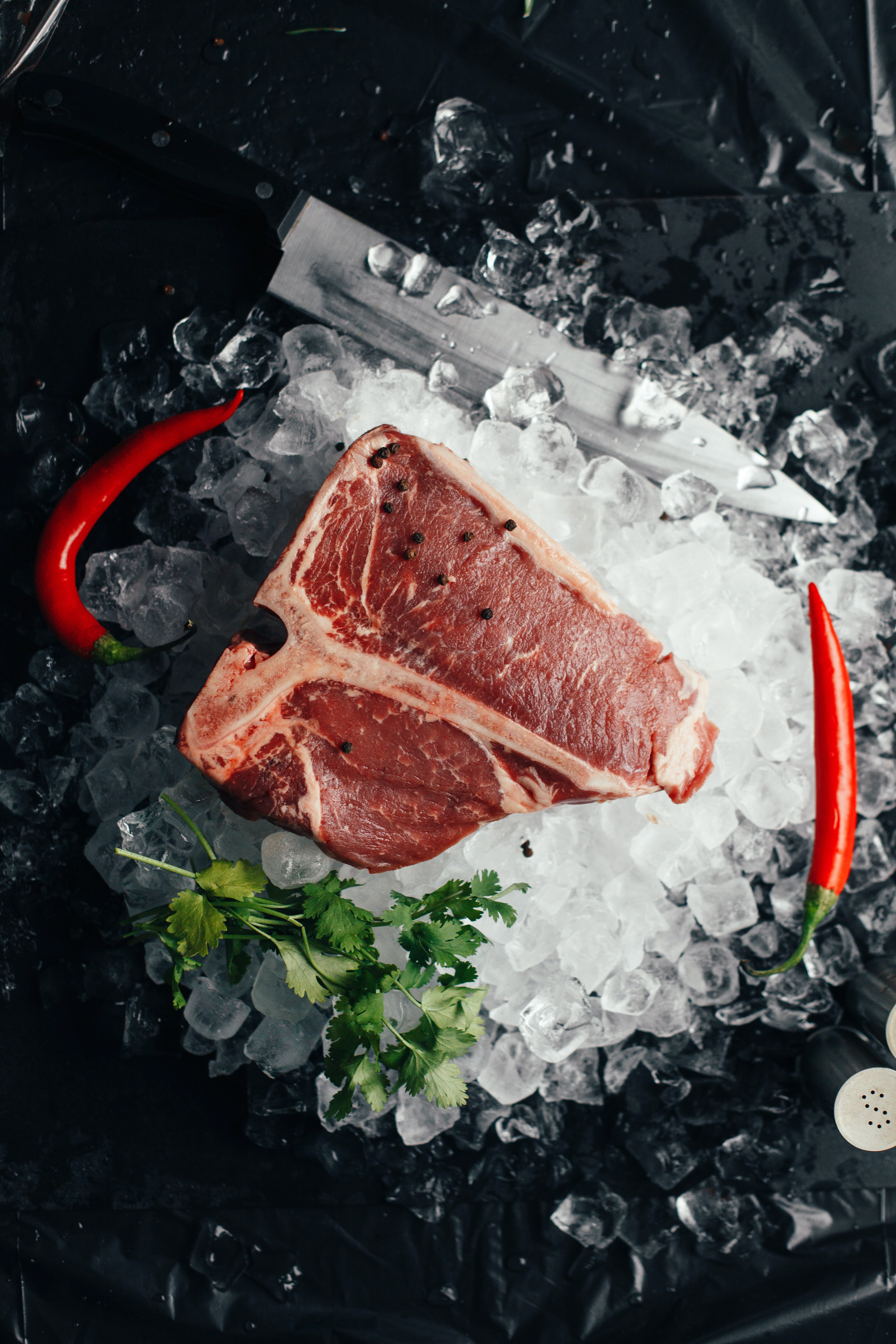 Raw T-bone steak on ice, accompanied by chili peppers and herbs, highlighting the use of soya protein concentrate