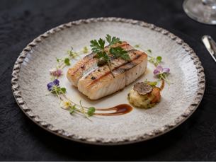 Gourmet fish fillet dish, garnished with brown sauce and edible flowers