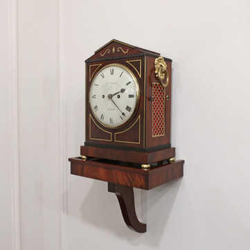 Antique English Regency mahogany small bracket clock with architectural shaped top and brass string inlay detail to the front by Thomas Connold striking the hours on a bell. The clock stands on a wall bracket