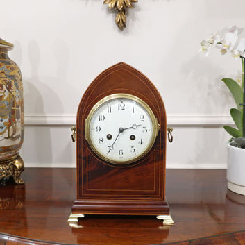 antique French Belle Epoque figured mahogany lancet top Edwardian period mantel clock with boxwood string inlay, brass axe head handles and brass bracket feet with eight day movement and Arabic numerals