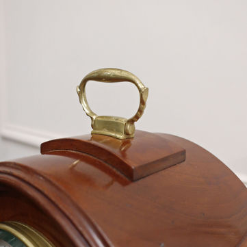 A small antique French Belle Epoque Victorian mahogany table clock with inset panels framed in brass moulding stood on brass ball feet and finished with a carrying handle to the top.