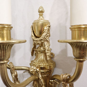An antique pair of French Edwardian Neoclassical Adams style bronze gilt wall lights with laurel leaf swags draped over the fluted three branches.