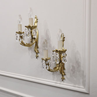 A pair of small early 20th century French Rococo style wall lights with twin arms and glass faceted pair drops hanging from each