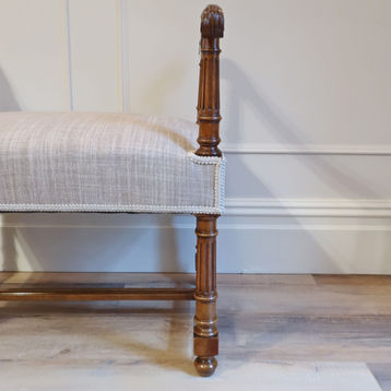 an antique French Edwardian period walnut window seat with leaf carvings to the arms and turned fluted columns upholstered in oatmeal beige linen fabric