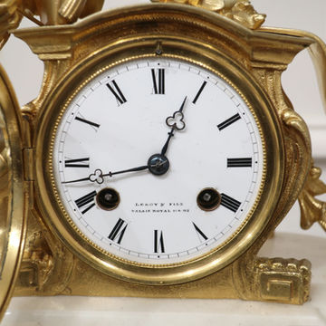 An antique French bronze gilt mantel clock with classical female figure wearing a dress writing in a book draped over a white carrara marble base by Leroy and stamped Dasson