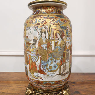A Japanese Meiji period satsuma porcelain table lamp with men, women and children in traditional dress with mountain scenes and birds. The lamp stands on a bronze base with elephants heads and was converted from oil by Hinks & Son