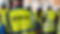 A group of construction workers at a project site in the back, wearing high-visibility vests with the 'NWFD - North West Fire Doors' insignia and protective helmets.