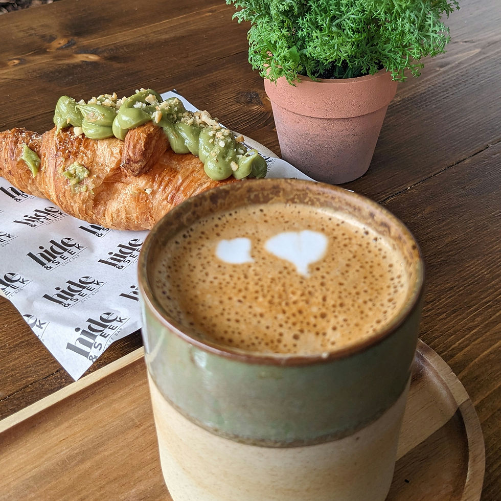Latte with heart foam pattern and croissant topped with green spread on tray at Hide & Seek Cafe Bar