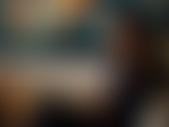 A professional hypnotherapist seated on a cream sofa writing session notes, with an abstract teal and gold artwork in the background, representing the thoughtful and personalized approach of Whole Brain Hypnotherapy training.