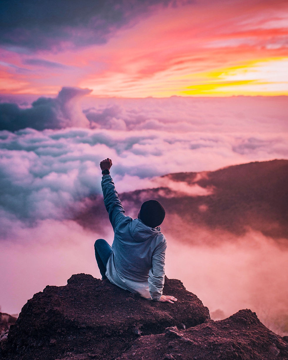 photo of man on top of a mountain holding his fist in the air celebrating success