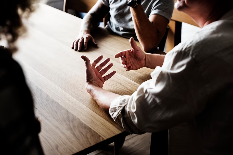 An image of three people sitting at a wooden table having a discussion