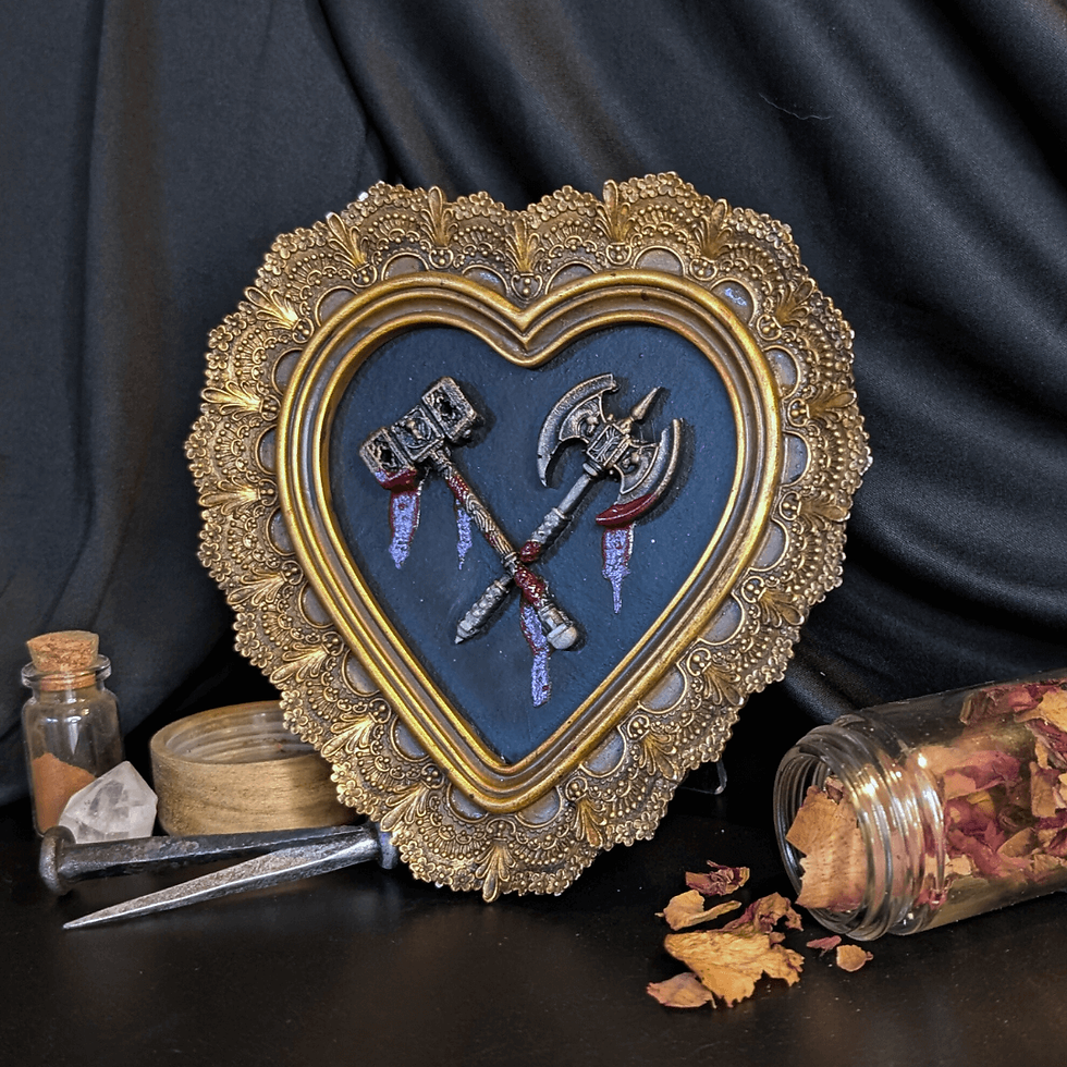 Heart-shaped frame with bloody weapons, nails, and rose petals displayed on table.
