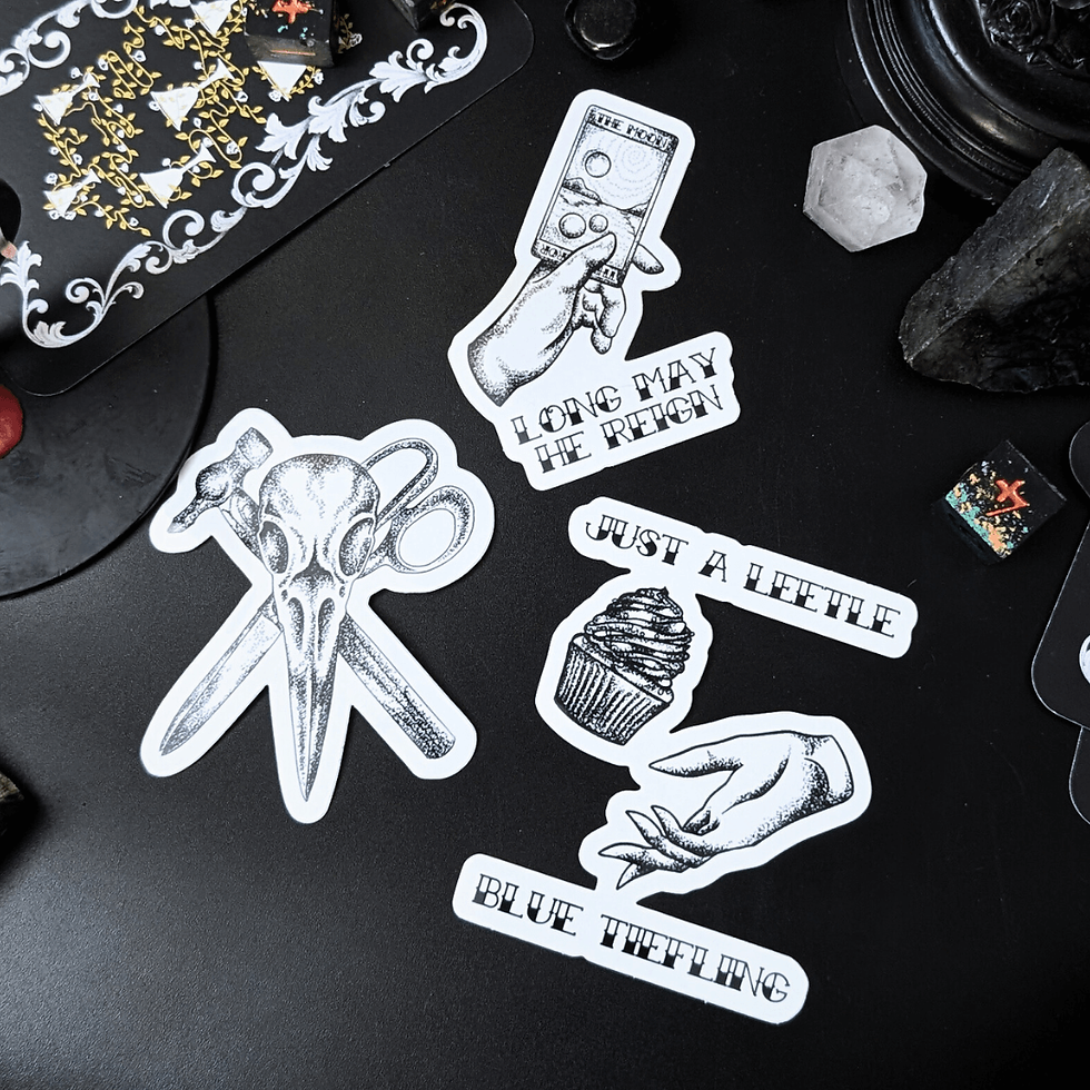 A set of three stickers; they are black and white linework artwork. One is a skull, one is a hand holding a tarot card, and one is a hand with a cupcake