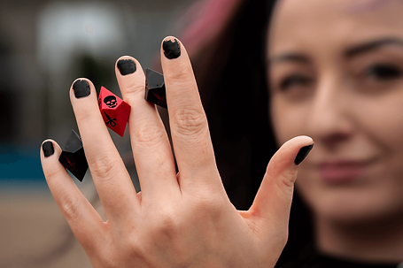 About Header Image | Roll Gothica | A set Vampire The Masquerade dice being held up inbetween fingers by the artist; Jodie