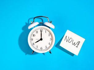 White alarm clock reading 10:10 and a note saying "NOW!" on a bright blue background. Energetic and urgent mood.