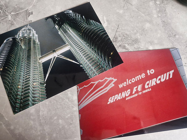 Weedon & Co. | The Petronas Twin Towers at night, showcasing the silver steel architecture and symmetry of Kuala Lumpur and the red entrance sign for the Sepang International F1 Circuit in Malaysia, representing the country's modern era.