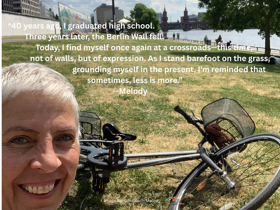 Life Coach Melody sitting on the grass with her bicycle and the Berlin Germany East Side Gallery Wall and the red Oberbaum Bridge in the background. With the words, “40 years ago, I graduated high school. Three years later, the Berlin Wall fell. Today, I find myself once again at a crossroads—this time, not of walls, but of expression. As I stand barefoot on the grass, grounding myself in the present, I’m reminded that sometimes, less is more.” --Melody