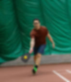 Man lunging to hit a pickleball with a black paddle.
