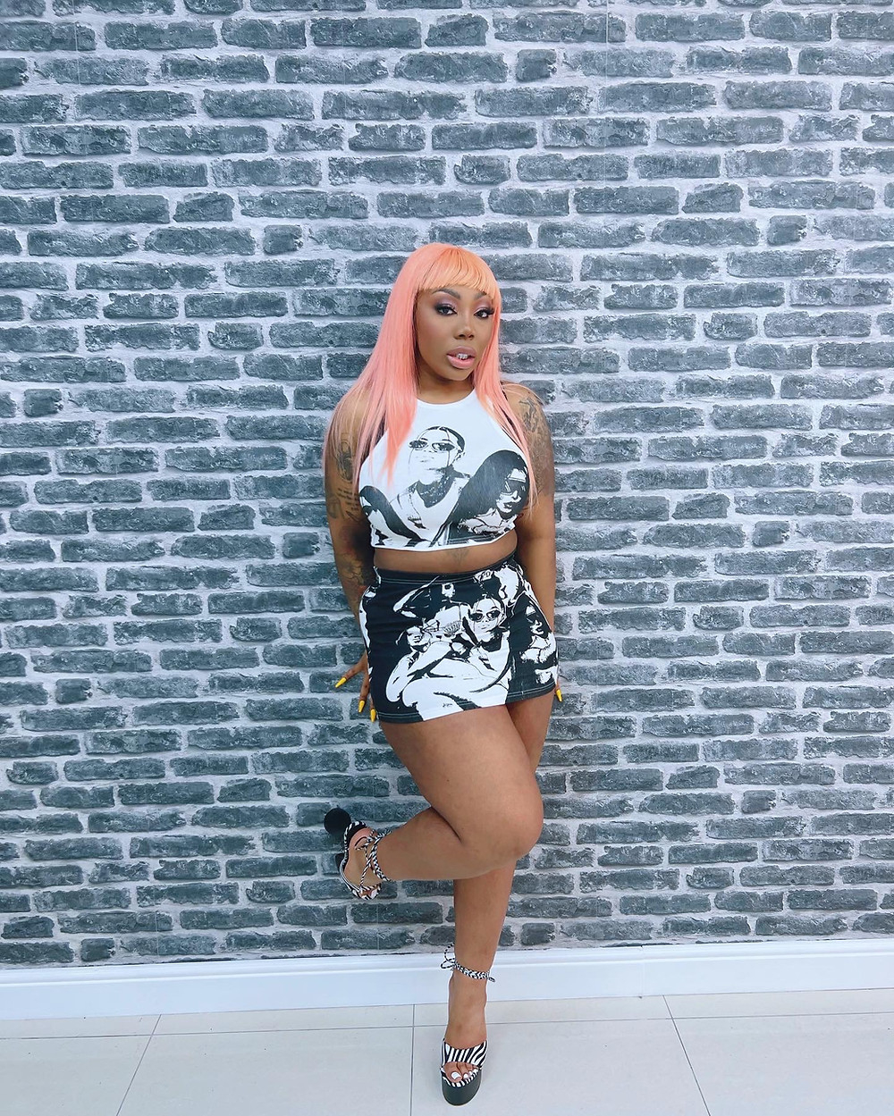 Eldé with pink hair leaning against a wall with heels