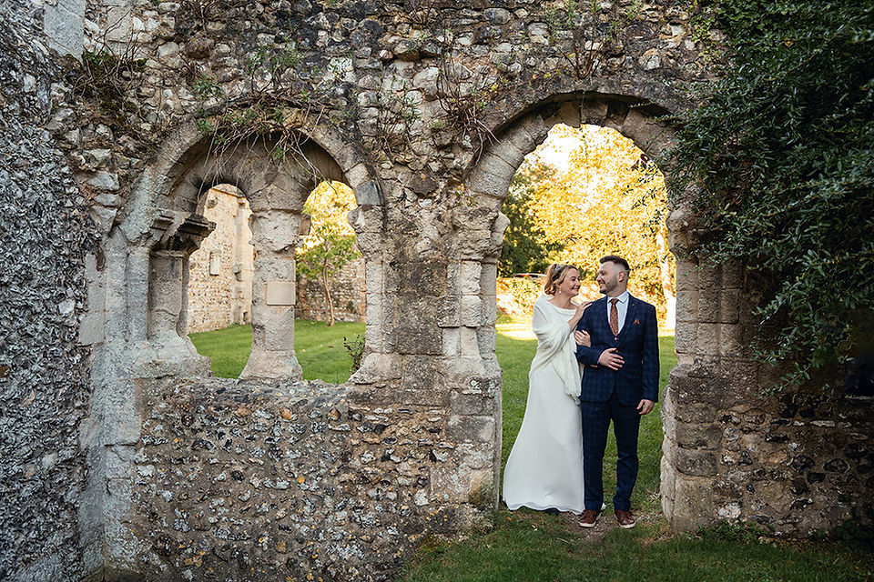 Bride and groom during a romantic wedding photo session at Boxgrove Priory Ruins in West Sussex, with the historic ruins and scenic countryside in the background.