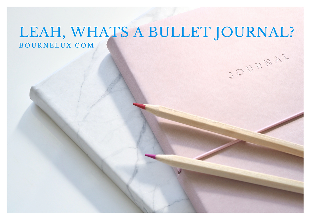 Two journals, one marble, one pink stacked on top of each other and then two coloured pencils on top, the words Leah, Whats a Bullet Journal? bournelux.co.uk are placed on top at the top of the image
