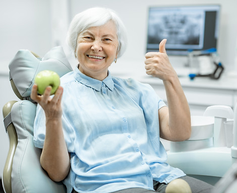 Portrait of a beautiful senior woman with healthy smile holding green apple at the dental