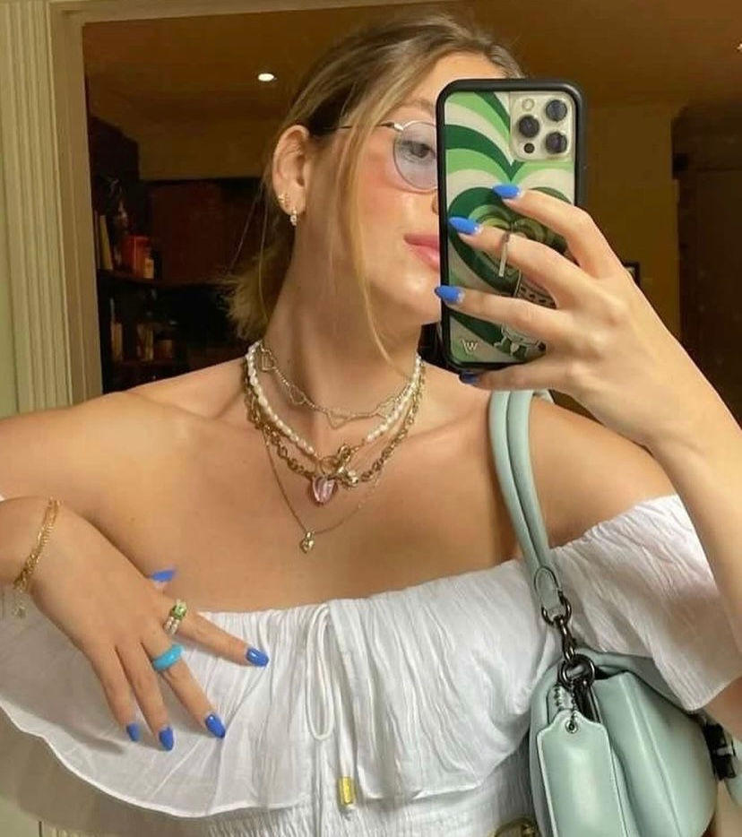 Thumbnail: A woman wearing a blue manicure and gold jewelries, holding a mint color bag taking a picuture