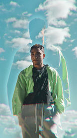 Young man in green jacket poses against a blue sky background