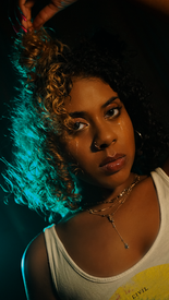 Young woman with curly hair poses for photo with a white tank top