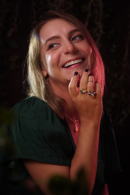 Smiling woman in green dress looking upwards with floral rings on her fingers.