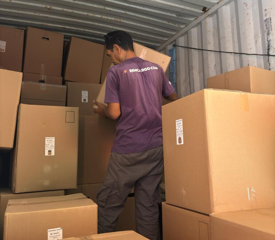 Rim's Staff arranging stacked cardboard boxes inside a shipping container, with labels visible.