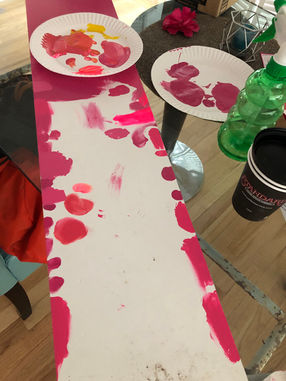 Hand mixing hot pink paint swatches on a white board