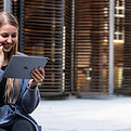 Woman in Westlake Village, California staring at apple tablet in front of modern, brown building.