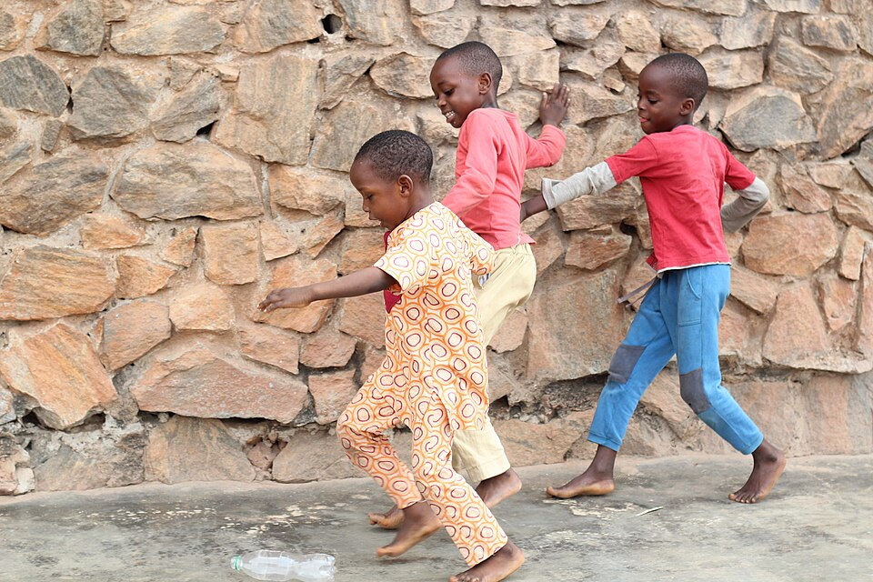 Three young children playing and running by a stone wall