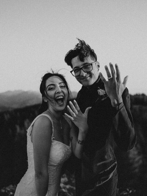A couple shows off their wedding rings with joy on their faces.