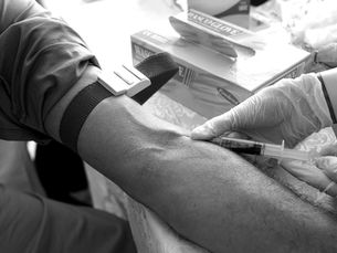 An arm with a tourniquet and blood being drawn; photo in black and white